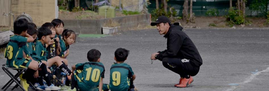 コーチが座りながら子供たちに指導している写真